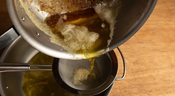 Braunes Butter wird durch ein Sieb gegossen, um die festen Bestandteile zu entfernen.