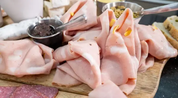 Dünn geschnittene Mortadella, eine italienische Brühwurst, liegt auf einem Holzbrett neben Salami und Oliven.