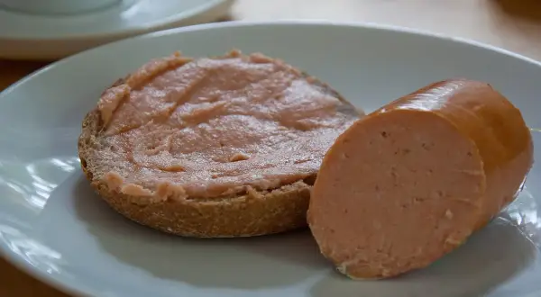 Ein Brötchen mit Teewurst und ein Stück Teewurst daneben. So sieht die beliebte Teewurst aus.