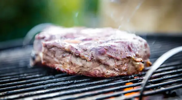 Ein saftiges Rindersteak grillen, Rauch steigt auf, die Flammen lodern darunter. Perfekt für den Grillabend!