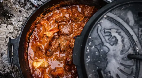 Herzhaftes Brauhaus Gulasch köchelt in einem gusseisernen Topf über glühender Asche. Ein Fest für die Sinne!