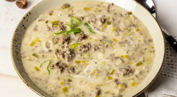 Eine cremige hackfleisch lauch suppe, garniert mit frischem Lauch und Gewürzen, serviert in einer rustikalen Schüssel.