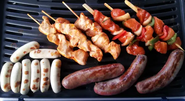 Fleisch auf Gasgrill richtig grillen: Hähnchenspieße und Würstchen brutzeln auf dem Grill.