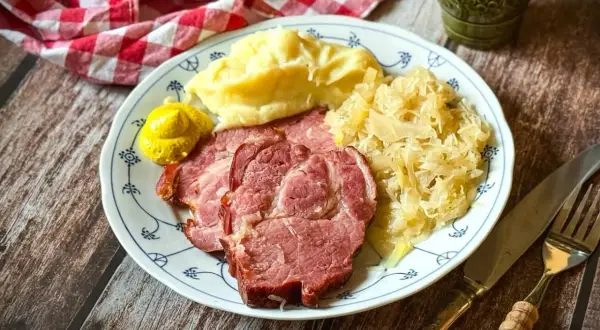 Kassler zubereiten: Saftige Scheiben Kassler mit Kartoffelpüree, Sauerkraut und Senf auf einem Teller. Ein deftiges Gericht, das man gerne isst.