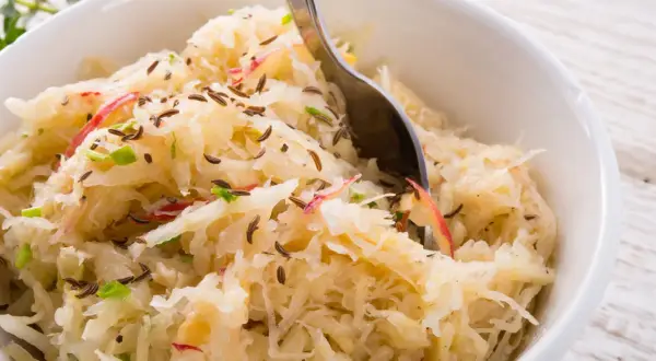 Schüssel mit Sauerkraut, verfeinert mit Kümmel und Apfelstücken. Eine Gabel ragt hinein, bereit zum Genießen.