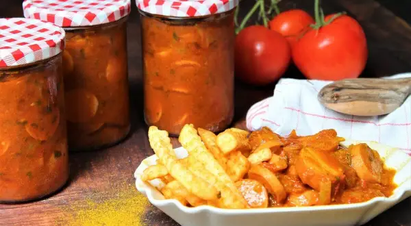 Gläser mit Currywurst-Sauce zum Einkochen, daneben eine Portion Currywurst mit Pommes.