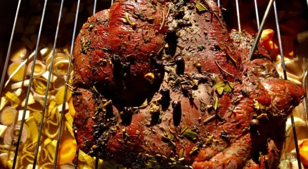 Ein saftiges Rehbraten mit Kräutern und Gewürzen wird auf einem Rost über Gemüse gegrillt.