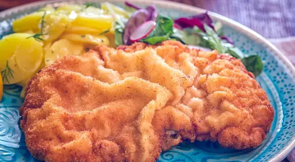 Goldbraunes Wiener Schnitzel mit Kartoffelsalat und frischem Grün. Ein perfektes Wiener Schnitzel Rezept für Genießer.