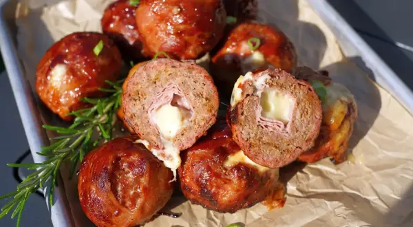Leckere "Moink Balls" mit geschmolzenem Käse und Schinken im Inneren, glasiert und auf einem Blech mit Rosmarin garniert.