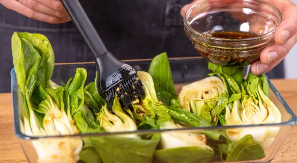 Marinade wird mit einem Pinsel auf halbierten Pak Choi aufgetragen, bereit zum **Pak Choi grillen**.