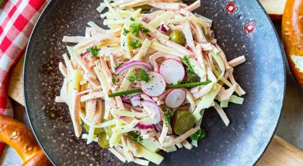 Ein herzhafter schweizer wurstsalat mit Käse, Radieschen, Gurken und Zwiebeln, garniert mit Petersilie.