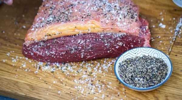 Ein roher Tafelspitz mit Salz und Pfeffer bestreut, bereit für das Tafelspitz grillen. Daneben eine Schale mit Pfefferkörnern.