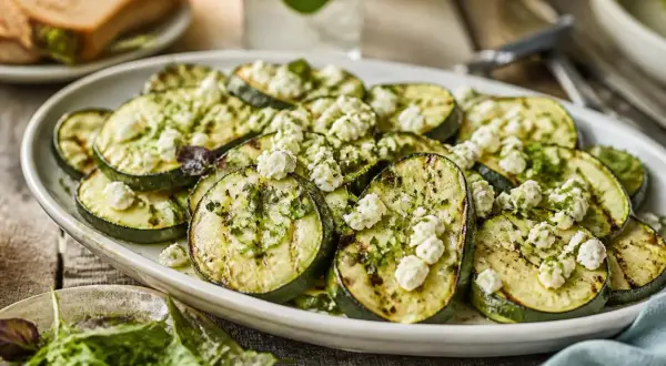 Gegrillte Zucchinischeiben mit zerbröseltem Feta und Kräutern, ein köstliches Gericht für den Sommer.