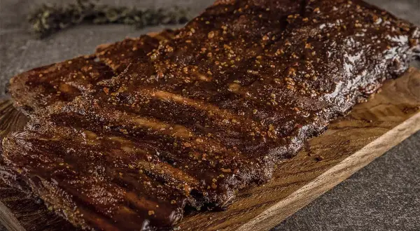 Saftige Rippchen vom Wildschwein, mariniert und perfekt gegrillt, liegen auf einem Holzbrett. Ein Genuss für jeden Grillmeister!