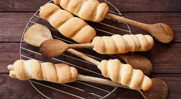 Goldbraunes Stockbrot-Rezept: Teig um Holzstäbchen gewickelt, auf einem Gitter abkühlen. Perfekt für Lagerfeuer!