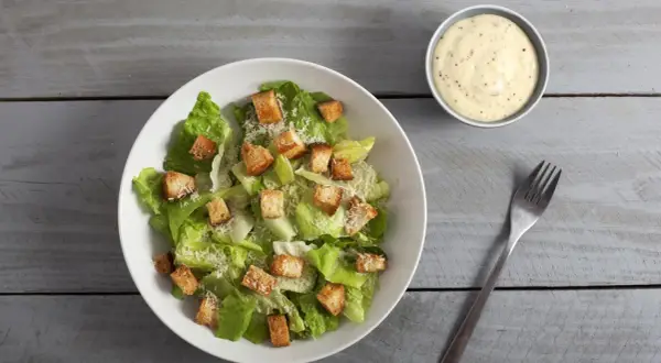 Frischer Caesar Salat mit knusprigen Croutons und Parmesan, dazu ein Schälchen cremiges Dressing.