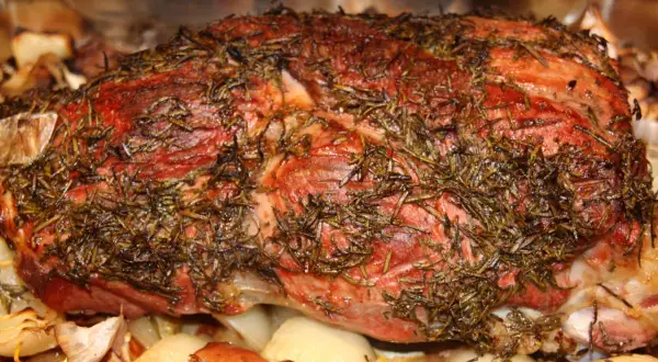 Saftige Lammkeule mit Rosmarin, bereit zum Grillen, liegt auf gerösteten Zwiebeln und Knoblauch.