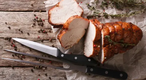 Saftiges braten fleisch, aufgeschnitten, mit Kräutern und Pfefferkörnern auf Holz. Messer und Fleischgabel liegen bereit.