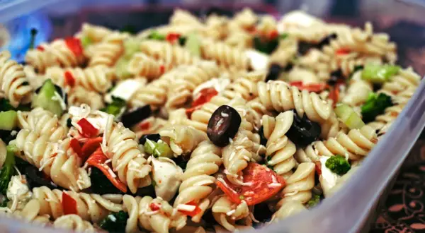 Ausgefallene Salate zum Grillen schnell gemacht: Nudelsalat mit Spiralnudeln, Oliven, Paprika und Brokkoli in einer Plastikschüssel.