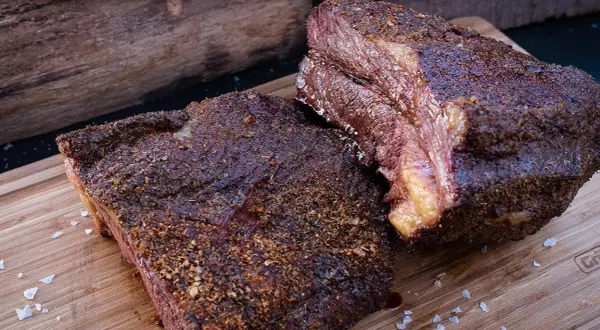 Zwei saftige Brisket-Stücke auf einem Holzbrett, bereit für die Messung der Kerntemperatur. Perfekt gegrillt!