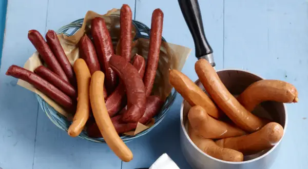 Bockwurst vs Bratwurst: Eine Auswahl an Würsten, einige dunkelrot in einem Korb, andere hellbraun in einem Topf.