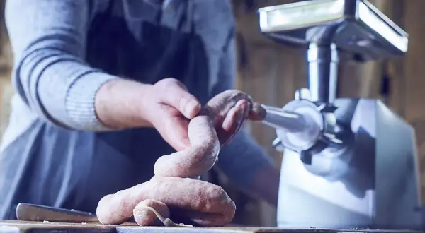 Mann stellt mit einer Wurstmaschine frische Würste her.