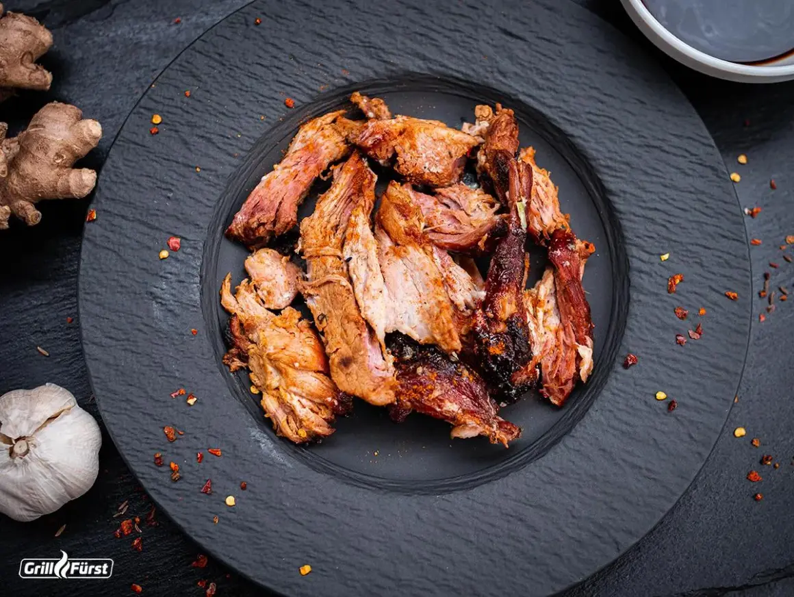 Zartes Pulled Pork auf schwarzem Teller, perfekt gegart. Die Kerntemperatur ist entscheidend für saftiges Fleisch. Ingwer und Knoblauch deuten auf würzige Aromen hin.