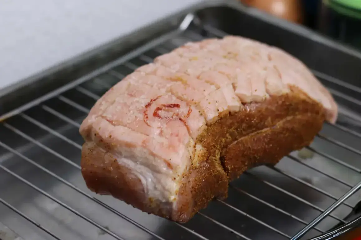 Ein Krustenbraten liegt auf einem Rost, bereit zum Krustenbraten grillen. Die Schwarte ist eingeschnitten und mit Gewürzen bestreut.