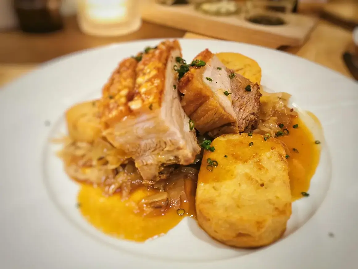 Saftiger Schweinebraten Niedrigtemperatur mit knuspriger Kruste, Kartoffelklößen und dunkler Soße auf einem weißen Teller.