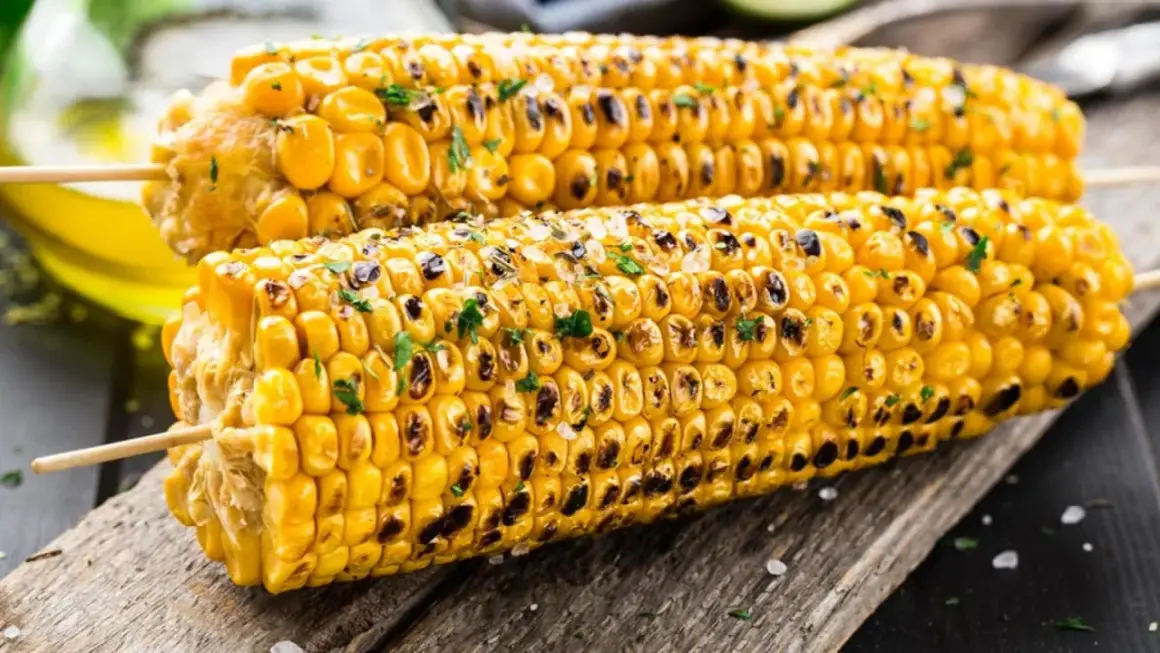 Zwei perfekt gegrillte Maiskolben mit gerösteten Stellen und Kräutern, bereit zum Genießen. Das Maiskolben grillen ist ein Sommergenuss.