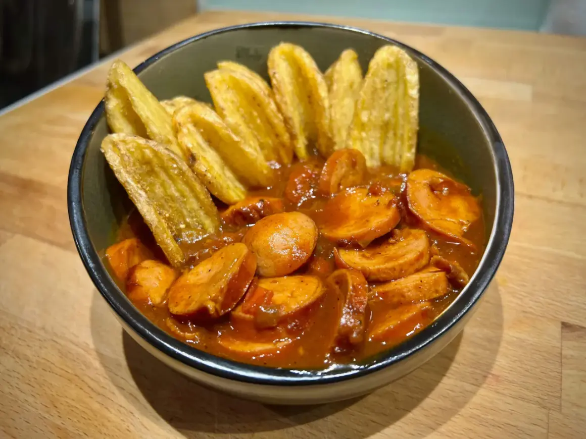 Eine Schüssel mit geschnittener Currywurst in Sauce und Kartoffelspalten. Perfekt für einen gemütlichen Abend, wie aus dem Dutch Oven.