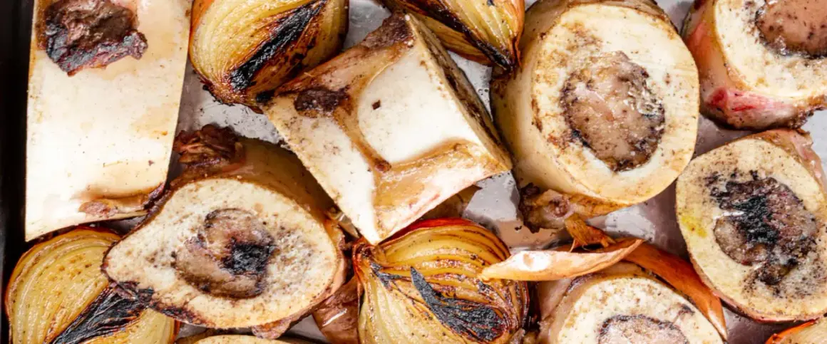 Geröstete Suppenknochen und Zwiebeln, bereit zum Kochen für eine herzhafte Brühe.