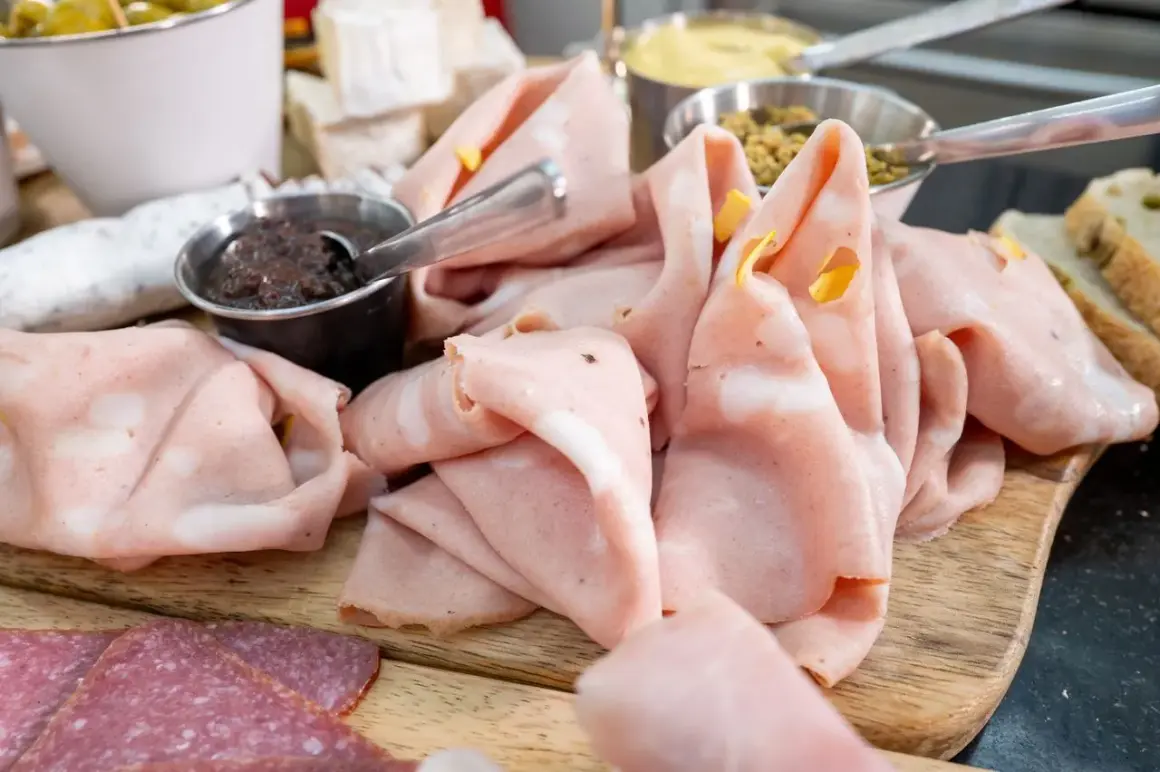 Dünn geschnittene Mortadella, eine italienische Brühwurst, liegt auf einem Holzbrett neben Salami und Oliven.