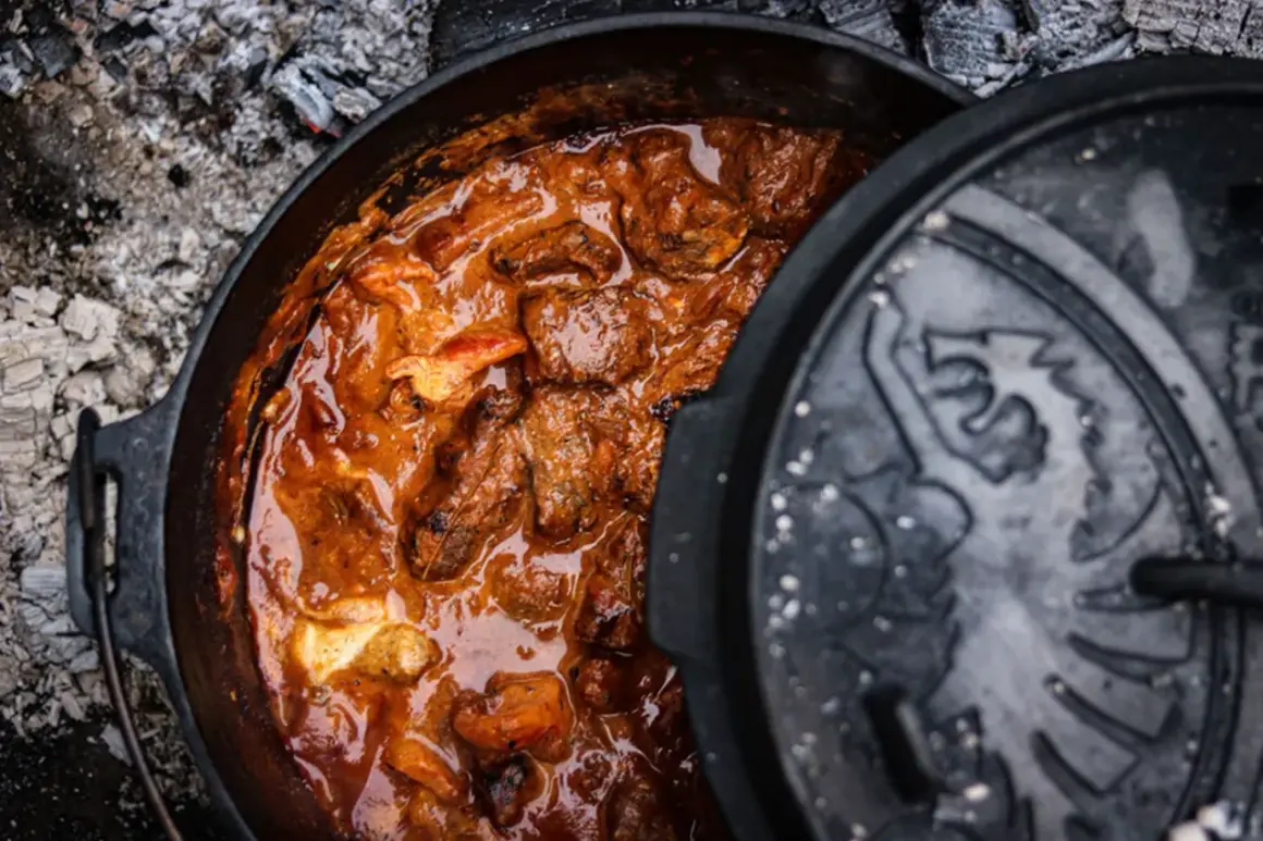 Herzhaftes Brauhaus Gulasch köchelt in einem gusseisernen Topf über glühender Asche. Ein Fest für die Sinne!