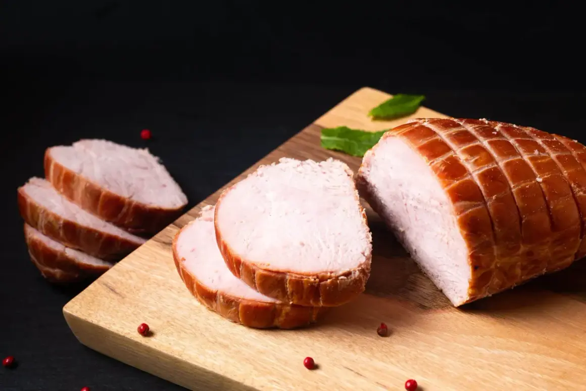 Ein aufgeschnittener Kassler-Braten mit perfekter Kerntemperatur, garniert mit Pfefferkörnern und Minze auf einem Holzbrett.