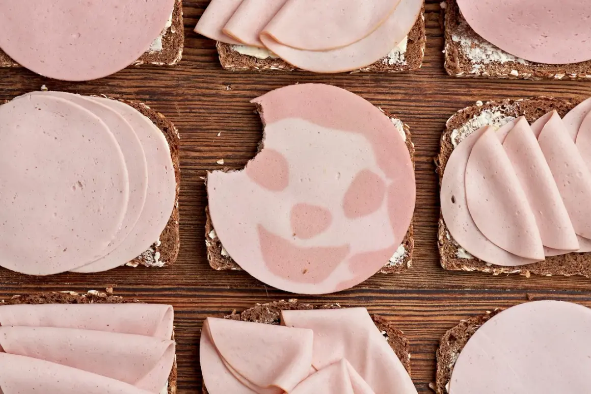 Biss in Lyoner: Welche Wurst ist gesund? Mehrere Brotscheiben mit Wurst belegt, liegen auf Holzuntergrund.