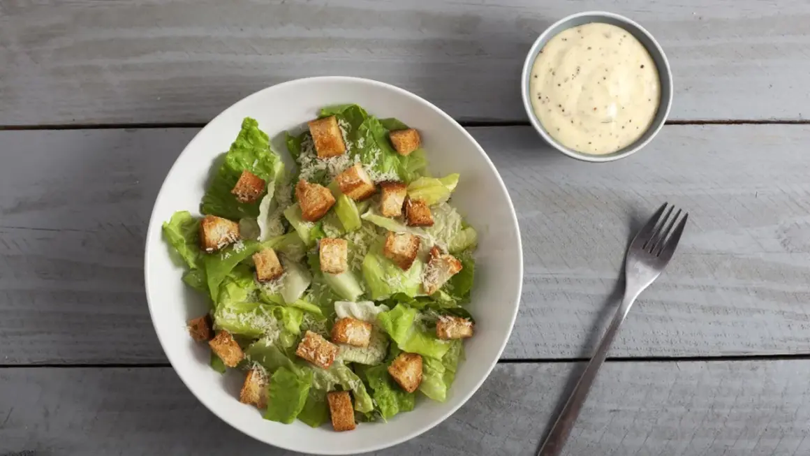Frischer Caesar Salat mit knusprigen Croutons und Parmesan, dazu ein Schälchen cremiges Dressing.