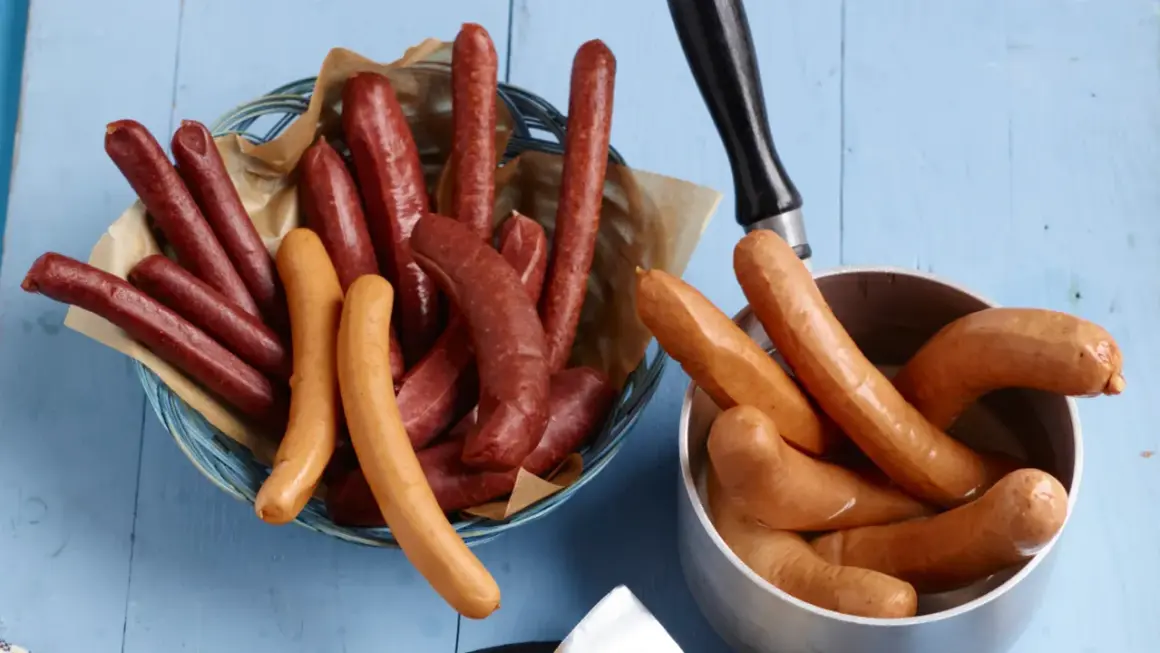 Bockwurst vs Bratwurst: Eine Auswahl an Würsten, einige dunkelrot in einem Korb, andere hellbraun in einem Topf.
