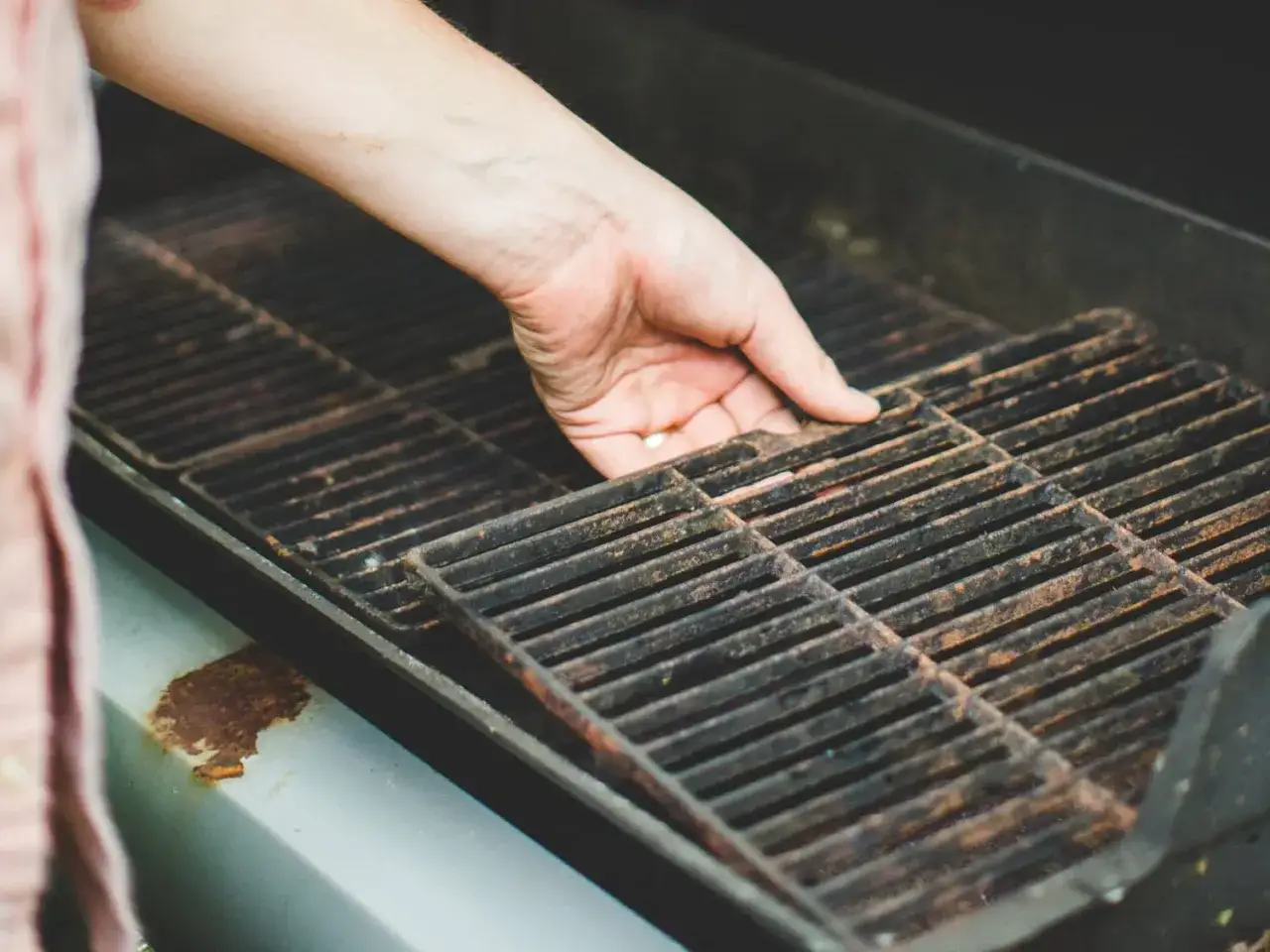 Hand entfernt Rost-bedeckte Grillroste, um das Grill ausbrennen vorzubereiten.