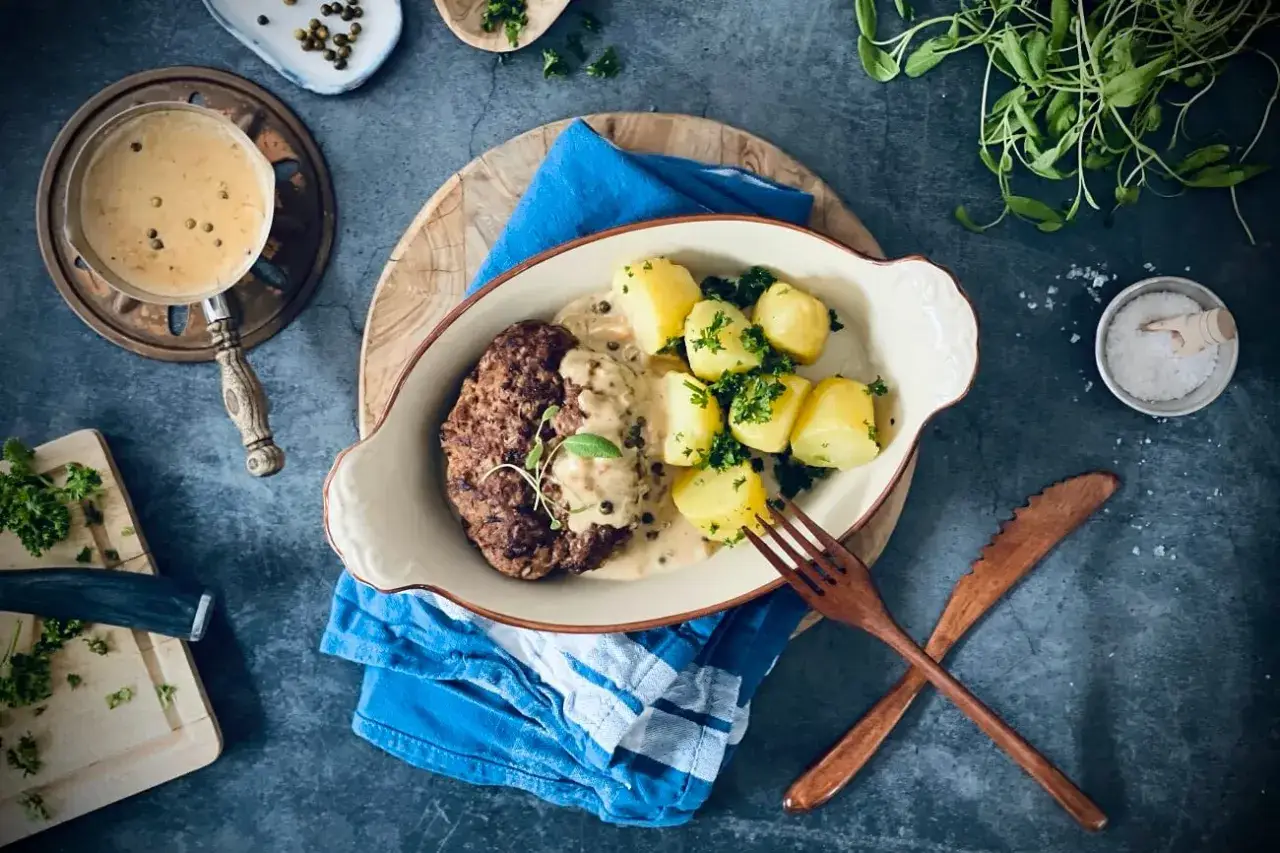 Hacksteak-Rezept: Ein saftiges Hacksteak mit cremiger Pfeffersauce und Salzkartoffeln, garniert mit frischer Petersilie. Ein Genuss!