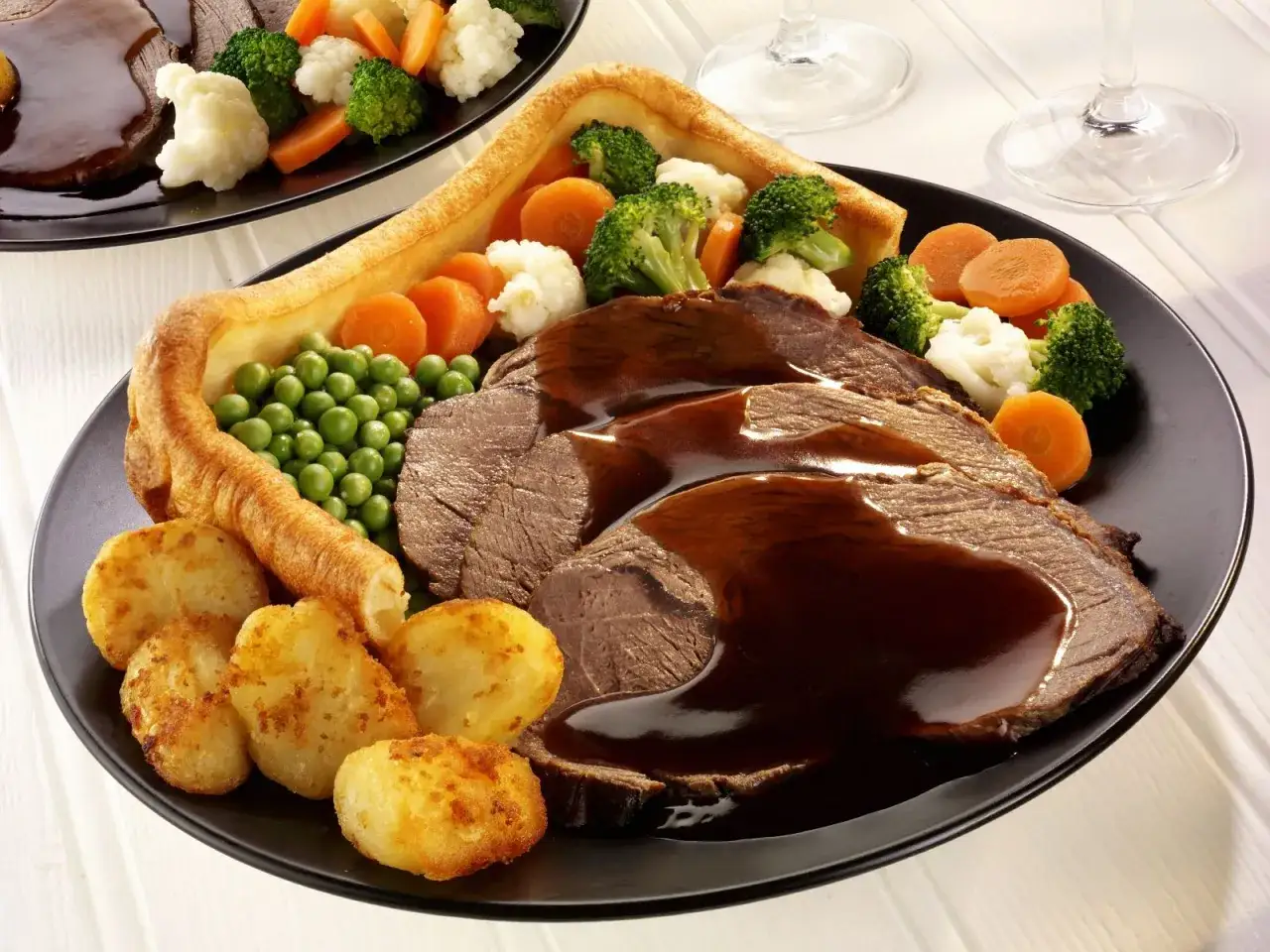 Ein Teller mit Braten, Bratkartoffeln, Erbsen, Gemüse und einem knusprigen Yorkshire Pudding, übergossen mit Soße.