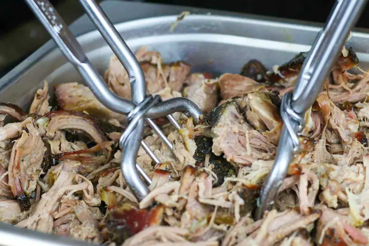Zangen zerreißen zartes pulled pork sous vide in einer Metallschale.