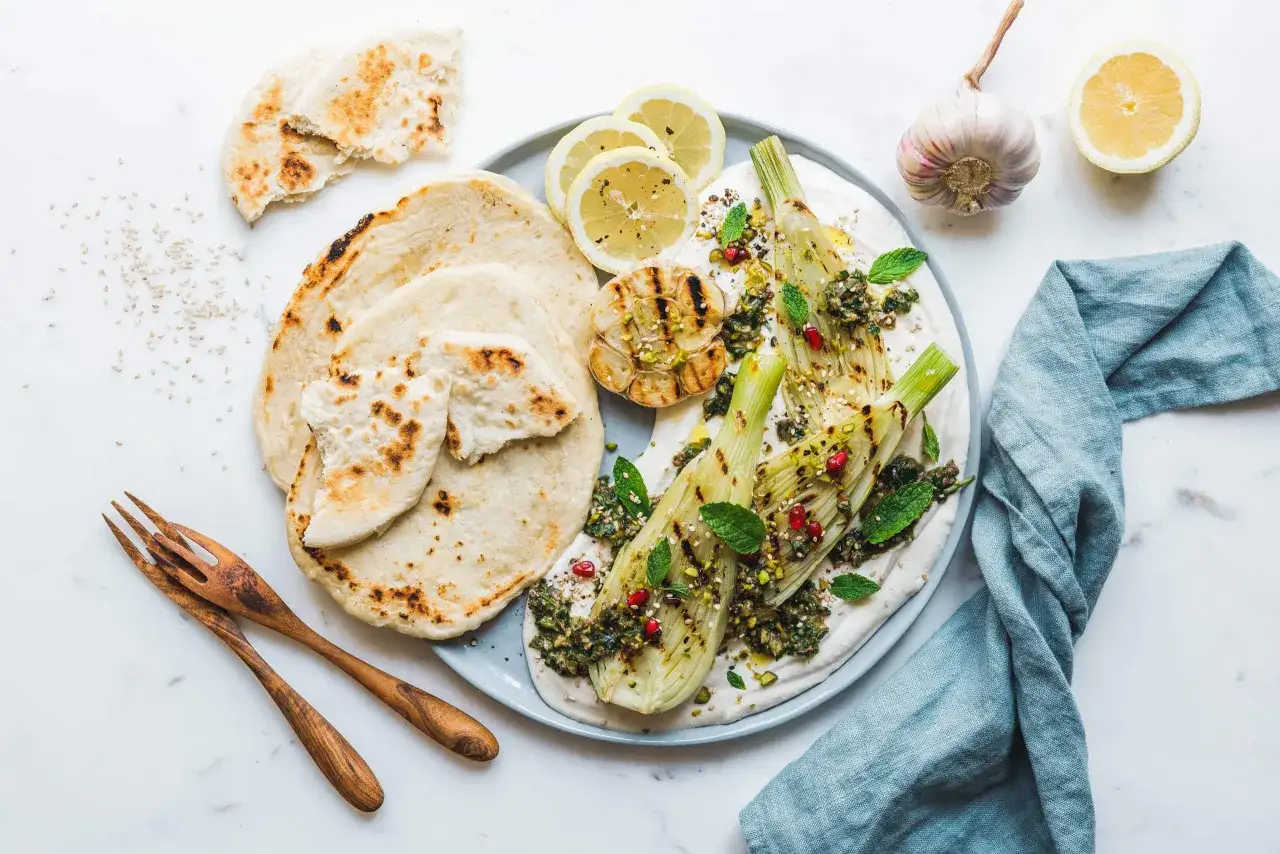 Gegrillter Fenchel auf cremiger Basis mit Granatapfelkernen, Pistazien und Minze, serviert mit Fladenbrot und Zitronenspalten.