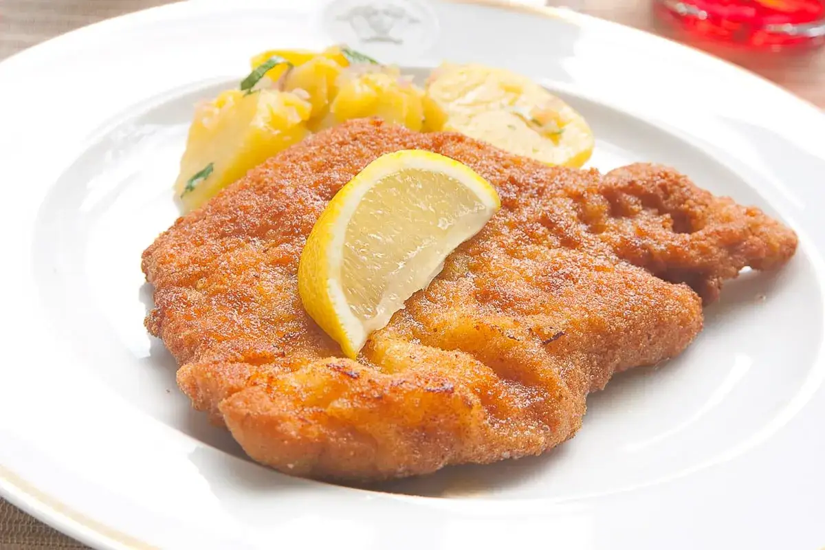 Ein knuspriges Wiener Schnitzel mit Zitrone und Kartoffelsalat. Perfekt für ein authentisches Wiener Schnitzel Rezept.