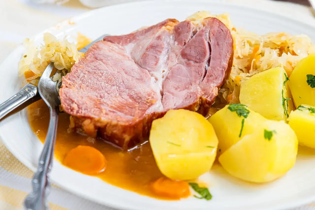 Ein saftiges Stück Kassler, zubereitet mit Sauerkraut und Salzkartoffeln, serviert auf einem Teller mit Soße und Karotten.