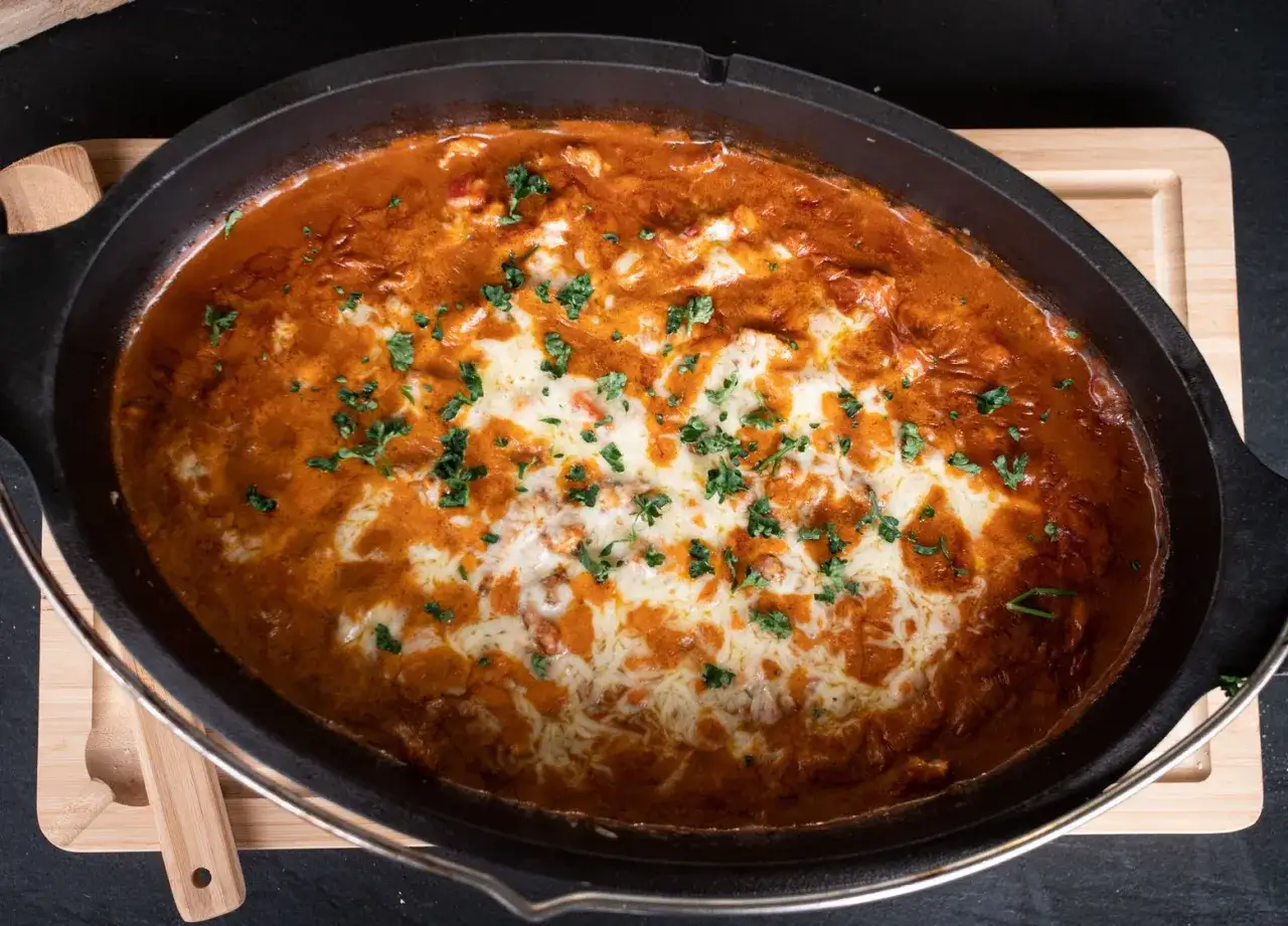 Herzhaftes Gyros-Gericht in einem Dutch Oven, überbacken mit geschmolzenem Käse und garniert mit Petersilie.