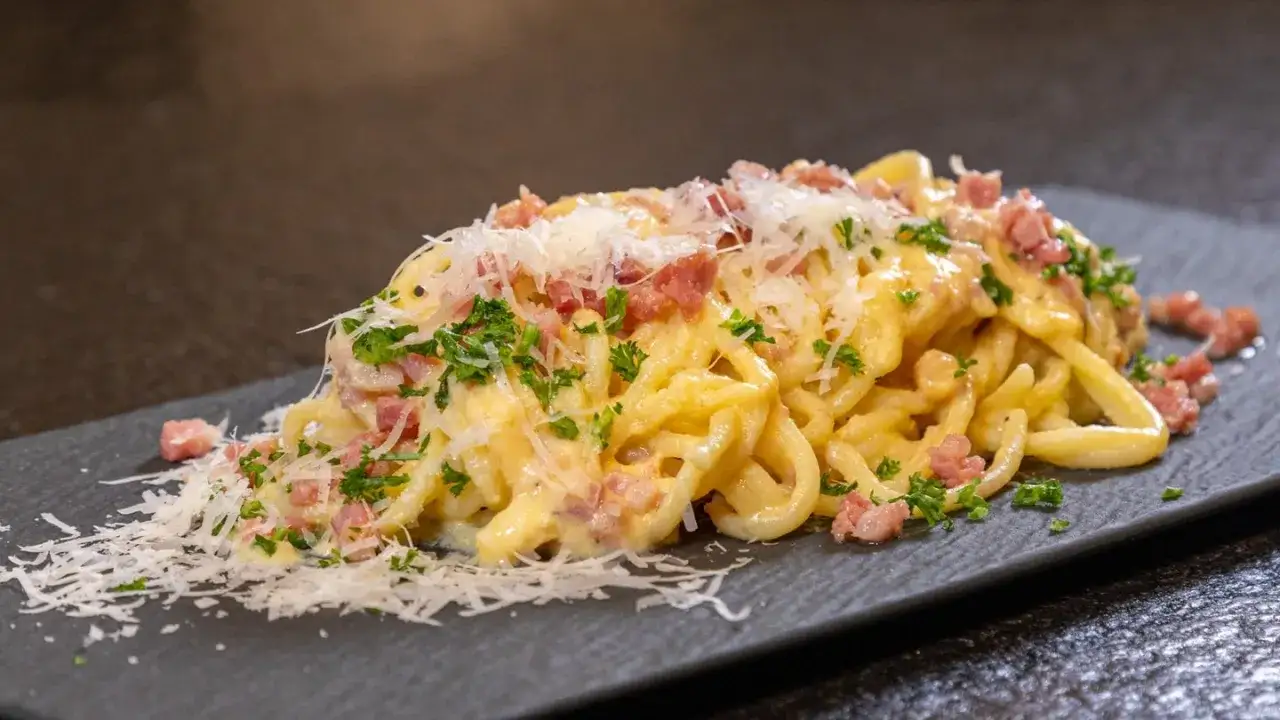 Ein Teller cremiger Spaghetti Carbonara, garniert mit Speckwürfeln, Petersilie und frisch geriebenem Parmesan.