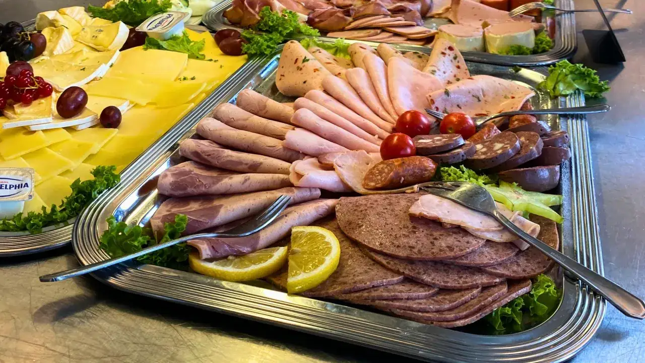 Vielfalt an Wurstsorten mit Bildern: Auf einem Silbertablett liegen verschiedene Aufschnitte, Käse, Trauben und Zitronenspalten.