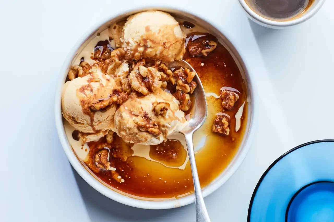 Eiscreme mit karamellisierten Walnüssen und einem Hauch von gebratenem Buttergeschmack. Ein Löffel wartet darauf, diese süße Köstlichkeit zu genießen.