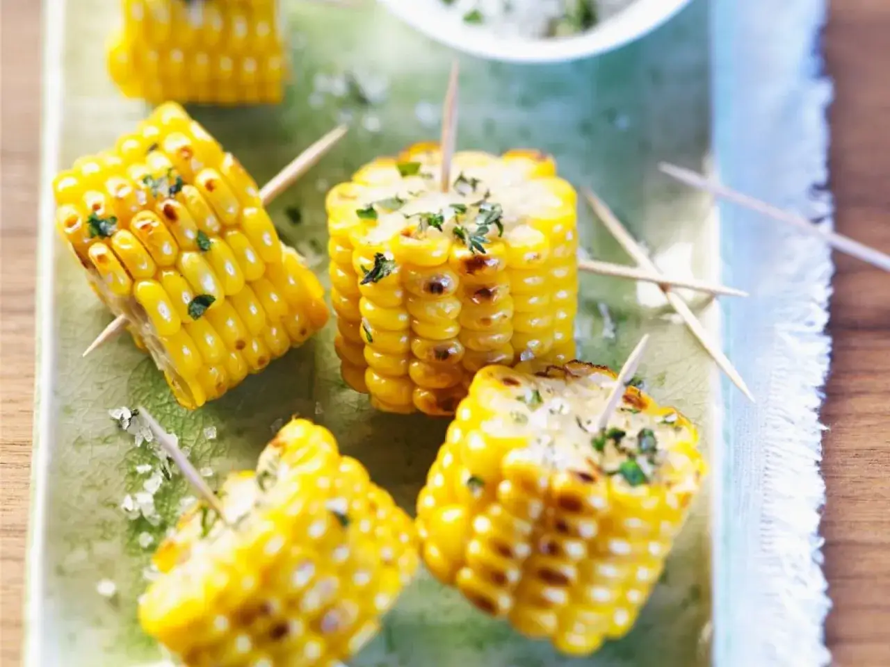Gegrillte Maiskolben-Stücke, gewürzt mit Kräutern und Salz, auf einem grünen Teller. Perfekt zum maiskolben grillen!